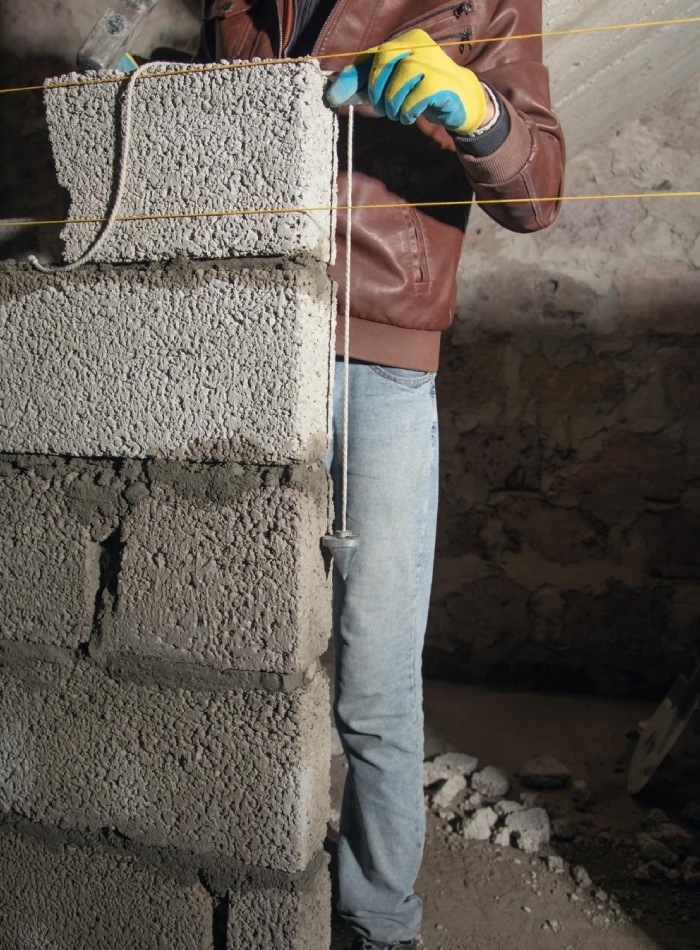 Contrôle de l’aplomb d’un mur en parpaings avec fil à plomb et cordeau de traçage